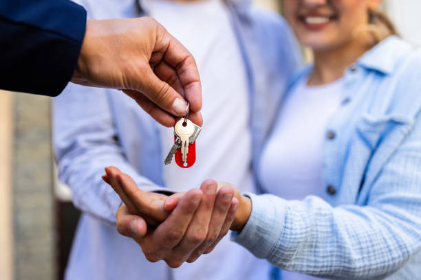 Real estate agent handing over keys to a young couple for their new home. Property ownership transfer complete.